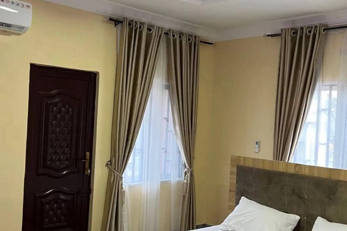 A hotel room with a bed, curtains, a wooden door, and a ceiling light.