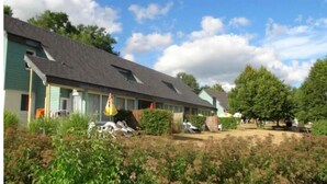 Une rangée de bâtiments d’un seul étage, dotés d’un toit en pente, qui semblent être un hôtel ou une auberge. On y trouve des espaces de détente en plein air avec des parasols, et les bâtiments sont entourés de verdure.