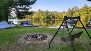 A lakeside camping area with a fire pit, a swing, and boats docked near the water. - Lake Nokomis cabin (Tomahawk)