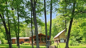 A cabin with a deck, surrounded by trees and a small pond. - Lake Nokomis cabin (Tomahawk)