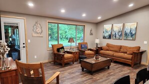 A spacious living room with a large window, wooden furniture, and artwork on the walls. - Lake Nokomis cabin (Tomahawk)
