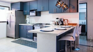 Una cucina moderna con mobili blu scuro, un'isola centrale con sgabelli da bar, elettrodomestici in acciaio inossidabile e illuminazione a sospensione.