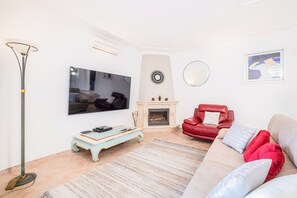 Ein Wohnzimmer mit Flachbildfernseher, Kamin, rotem Ledersofa und Stehlampe.