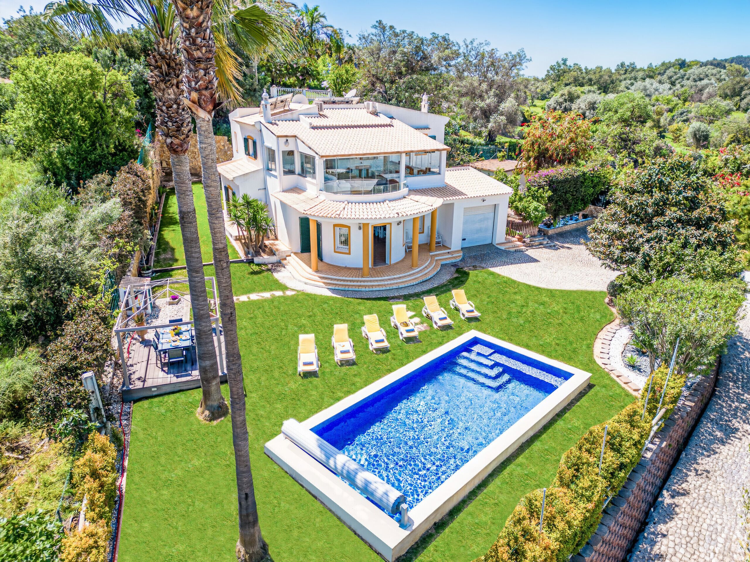 Una amplia casa de varios pisos con piscina, rodeada de un césped cuidado y palmeras.