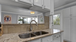 A kitchen with white cabinets, granite countertops, a stainless steel sink, and a window with a view of trees.