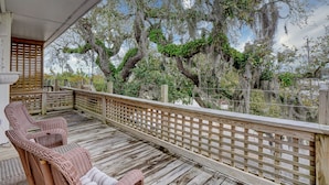 A wooden deck with wicker furniture and a view of trees with Spanish moss.