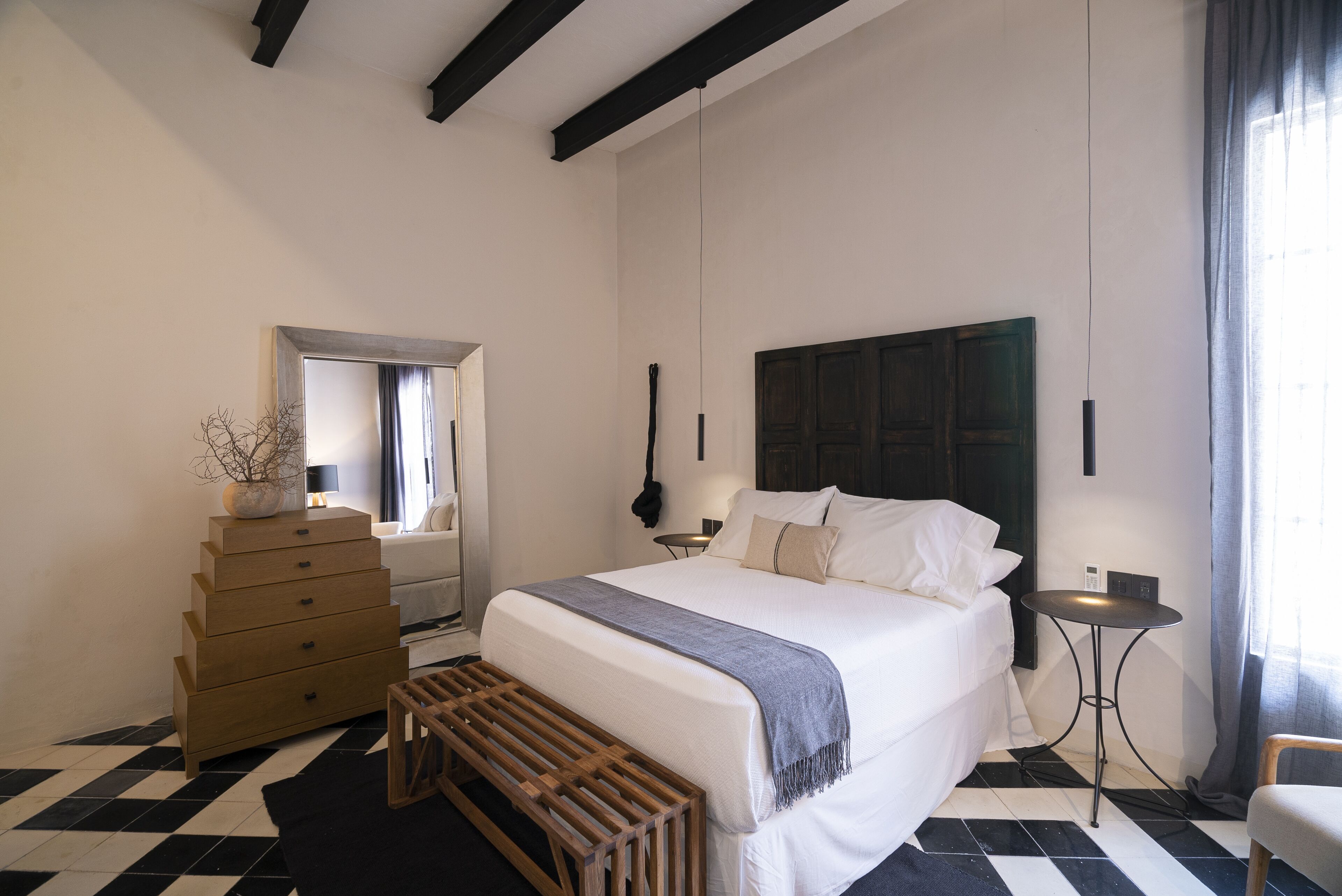 Un dormitorio con cama, cómoda, banco, una mesita y un espejo.