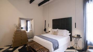 Un dormitorio con cama, cómoda, banco, una mesita y un espejo.