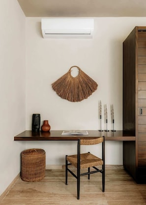 Ein Zimmer mit einem Holztisch, einem Gewebestuhl, einem Korbwannenkorb, einer Wand-Klimaanlage und einem Holzkasten.