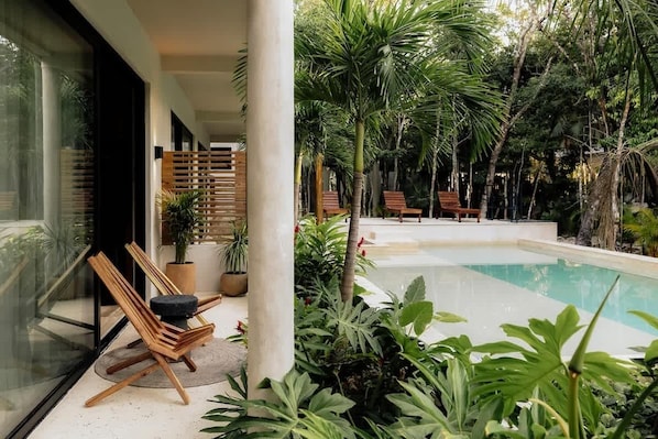 Ein Poolbereich mit Holzterrasse, Liegestühlen und tropischer Bepflanzung.