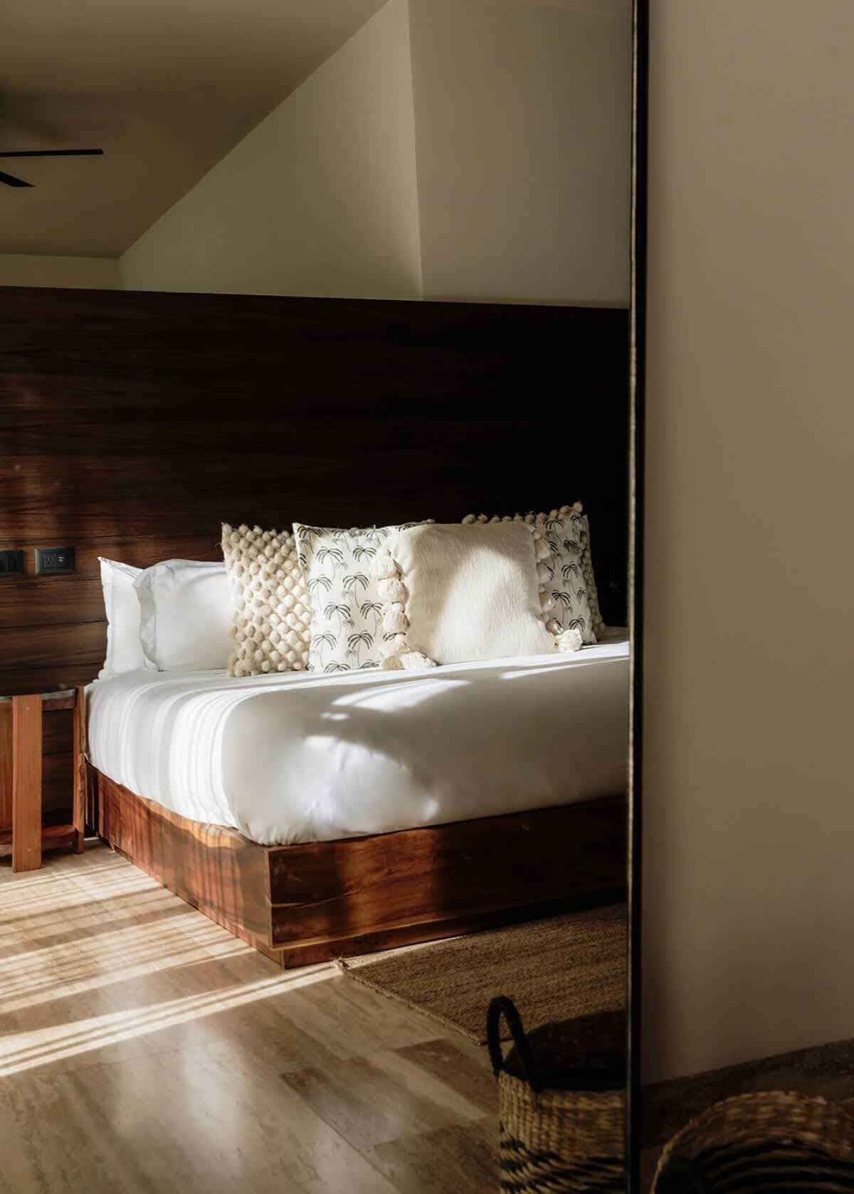 Una camera da letto con un letto in legno, biancheria da letto bianca e un cuscino decorato.