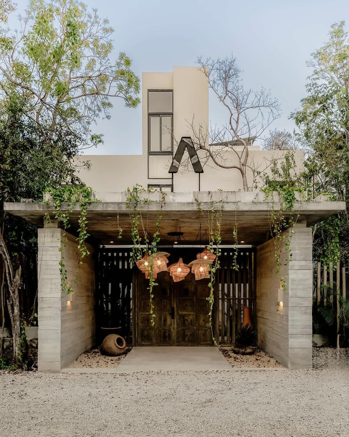 A modern building with a large 'A' logo, a covered entrance with hanging lights, and a gravel driveway.