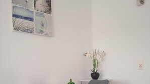 A dining area with a white table, two black chairs, a vase with white flowers, and a wall-mounted light fixture.