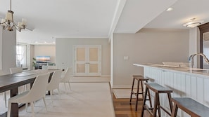 A modern kitchen with a bar area, white cabinetry, and a dining area with a table and chairs. - Oceanfront 3BR Residence with Wraparound Veranda (Wildwood)