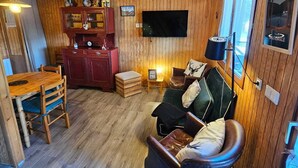 Een gezellig chalet interieur met houten plafond, een aan de muur bevestigde televisie, een houten eettafel met stoelen en een leren bank.