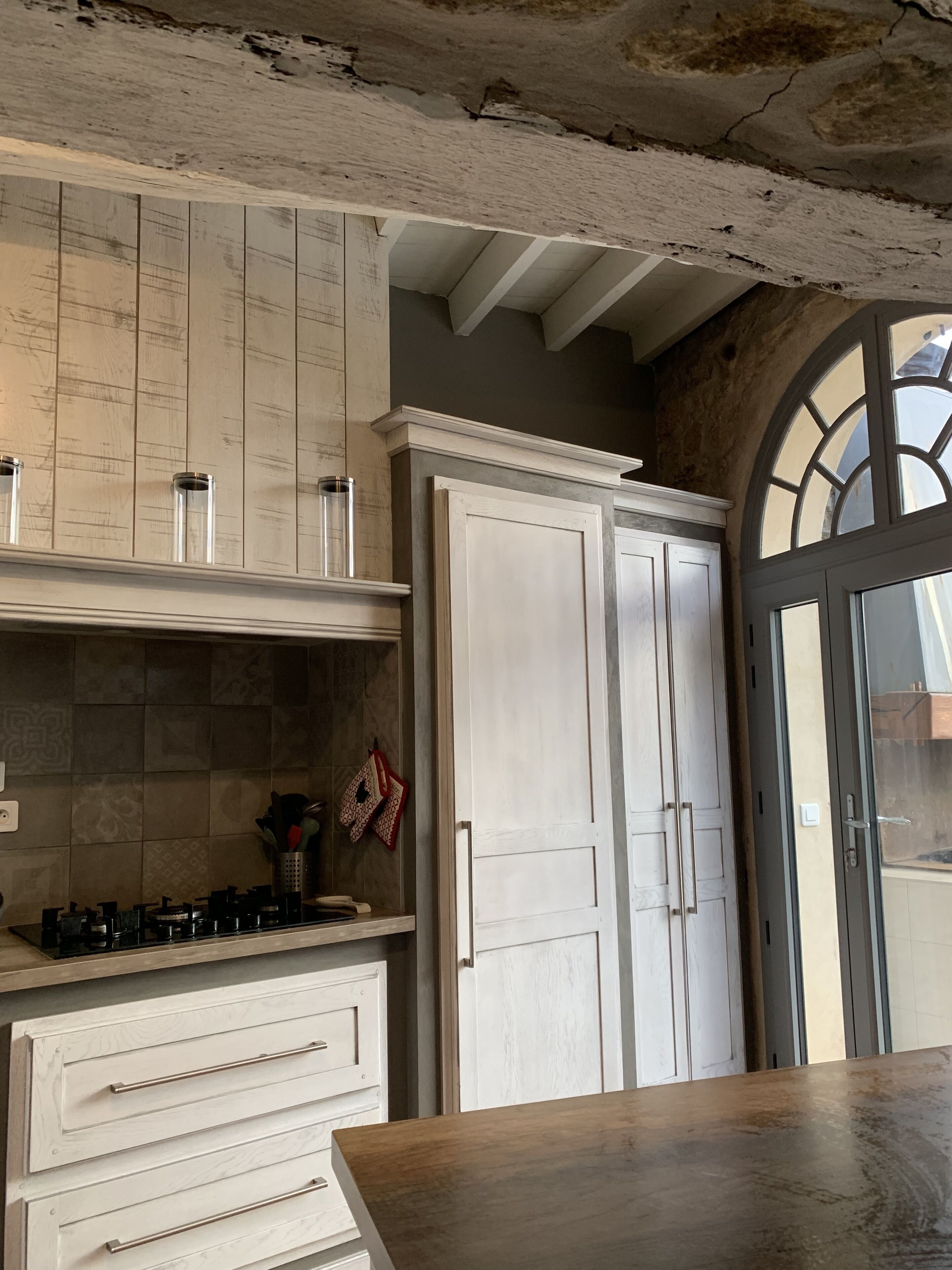 A kitchen with white cabinetry, a wooden countertop, and a view through an arched window.