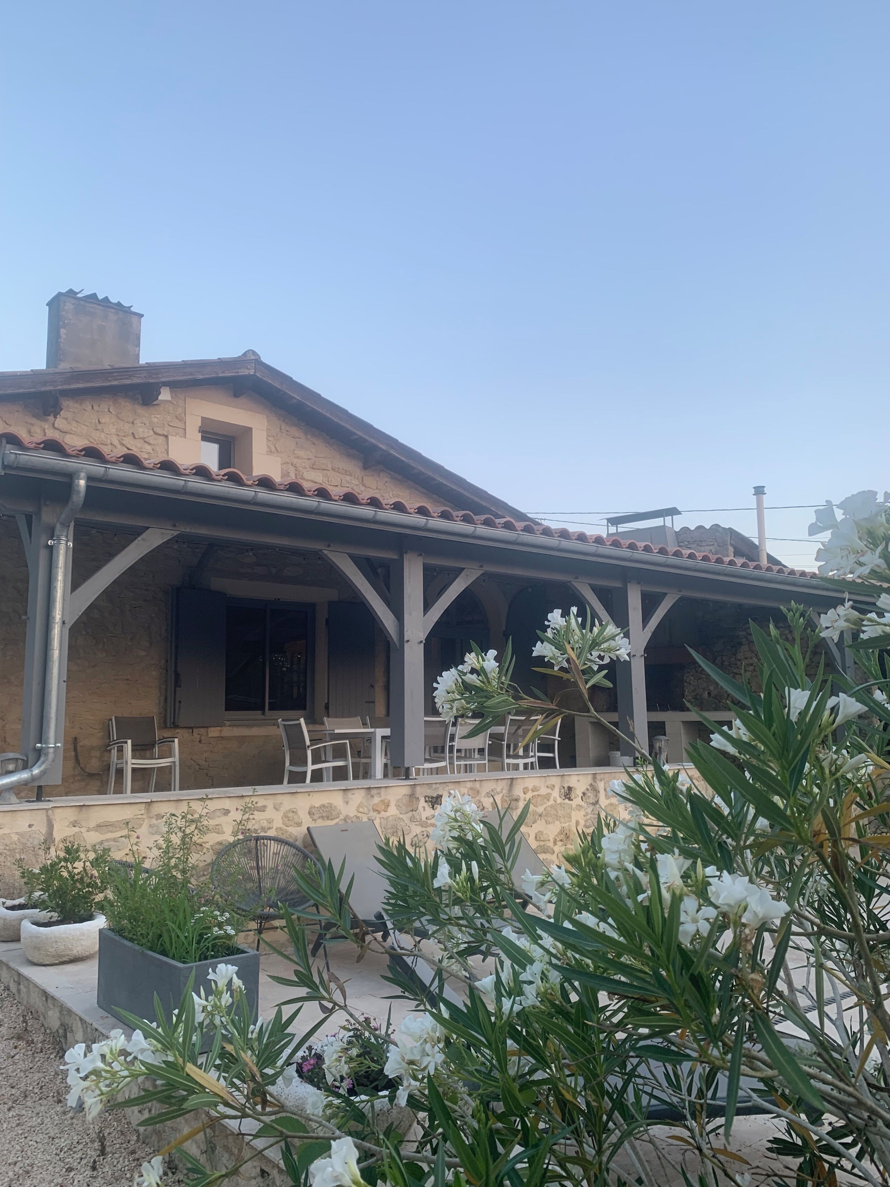 Um edifício com fachada de pedra, telhado de telhas e um terraço coberto com cadeiras.