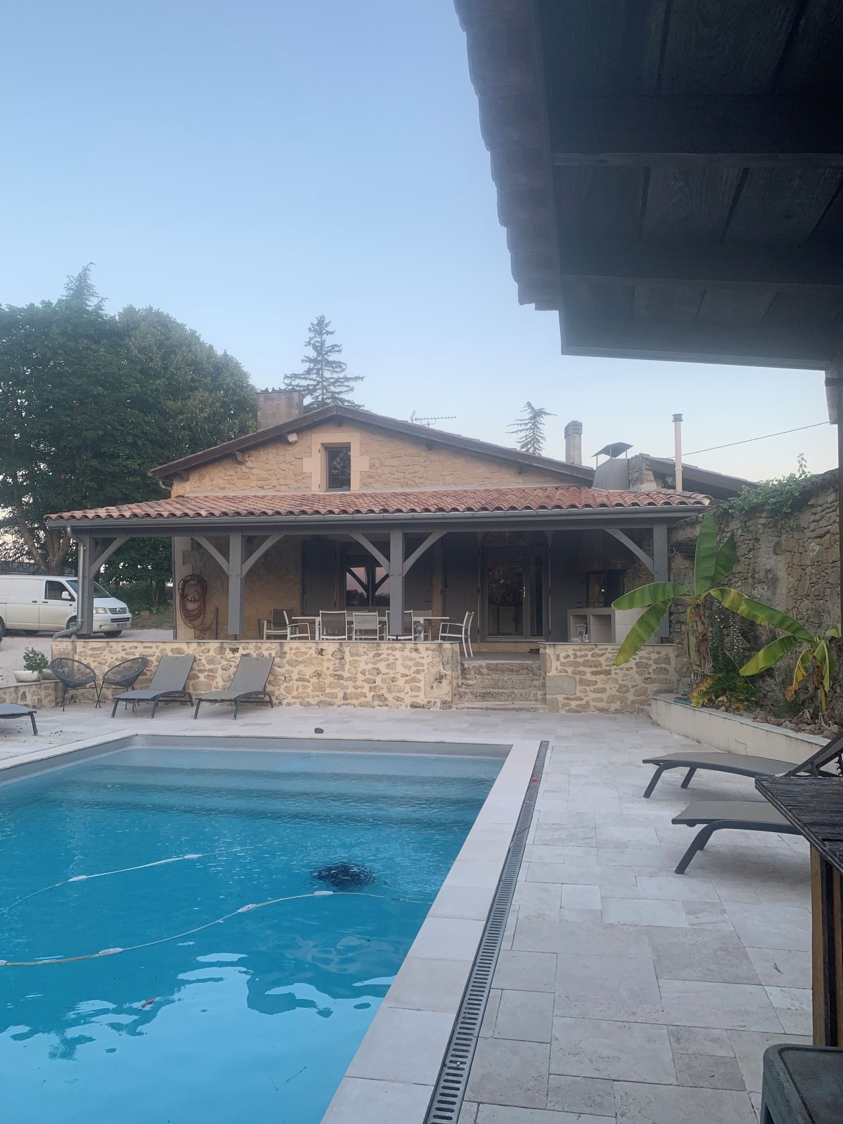 Un edificio in pietra con tetto in tegole, piscina e area salotto all'aperto.