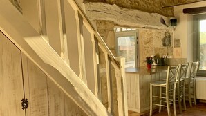 Eine rustikale Küche mit einer Holztreppe, Steinwänden und Blick ins Freie.