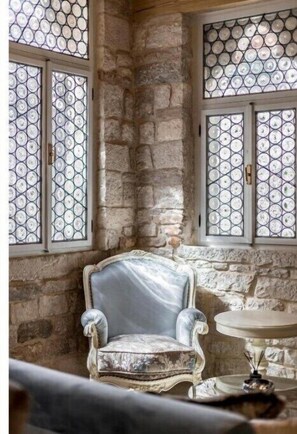 Classic design meets traditional style in this elegant room, featuring a stone wall, large windows, plush armchair, and small round table.