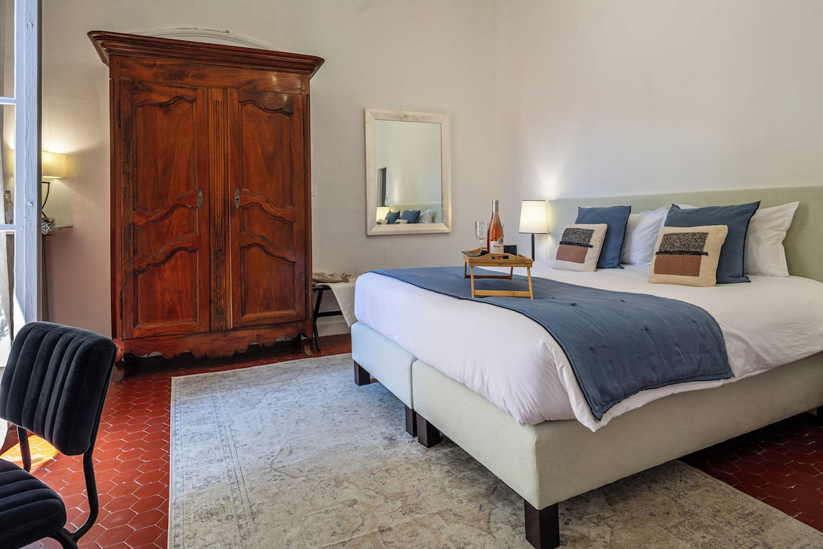 Een slaapkamer met een grote houten garderobe, een bed met een blauwe deken, en een spiegel aan de muur.