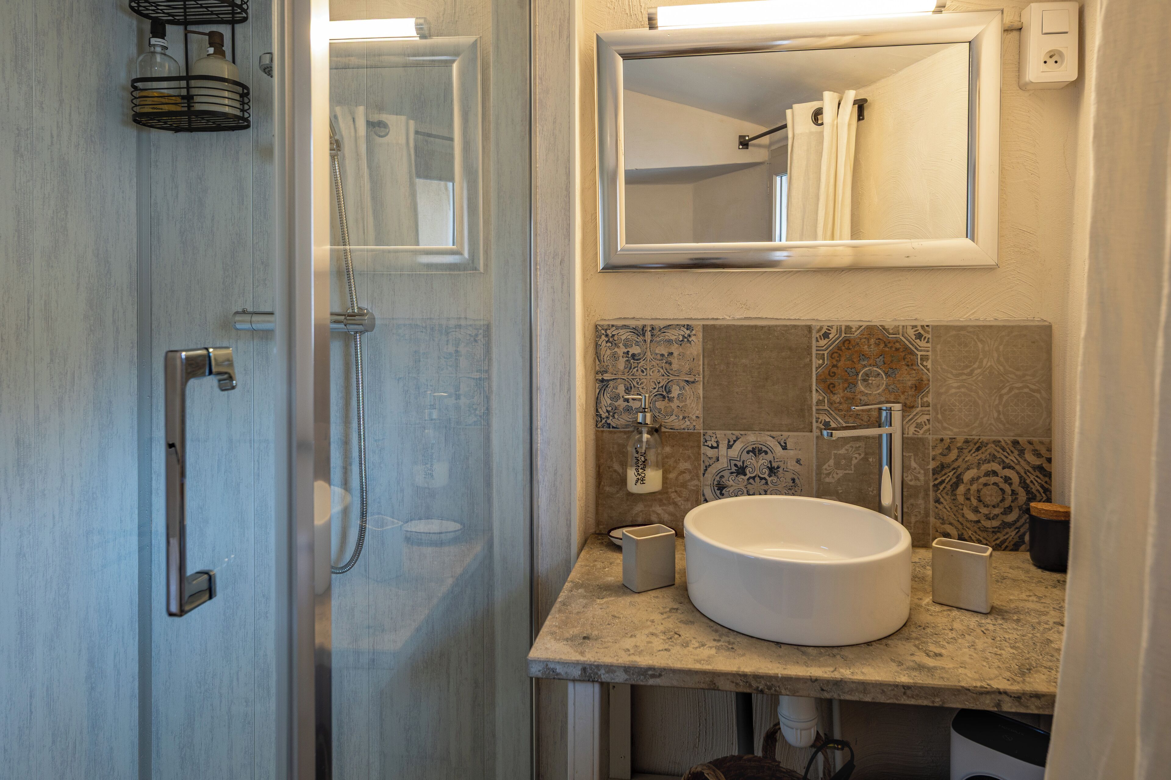 A bathroom with a glass shower door, a sink with a mirror above it, and a tiled backsplash.