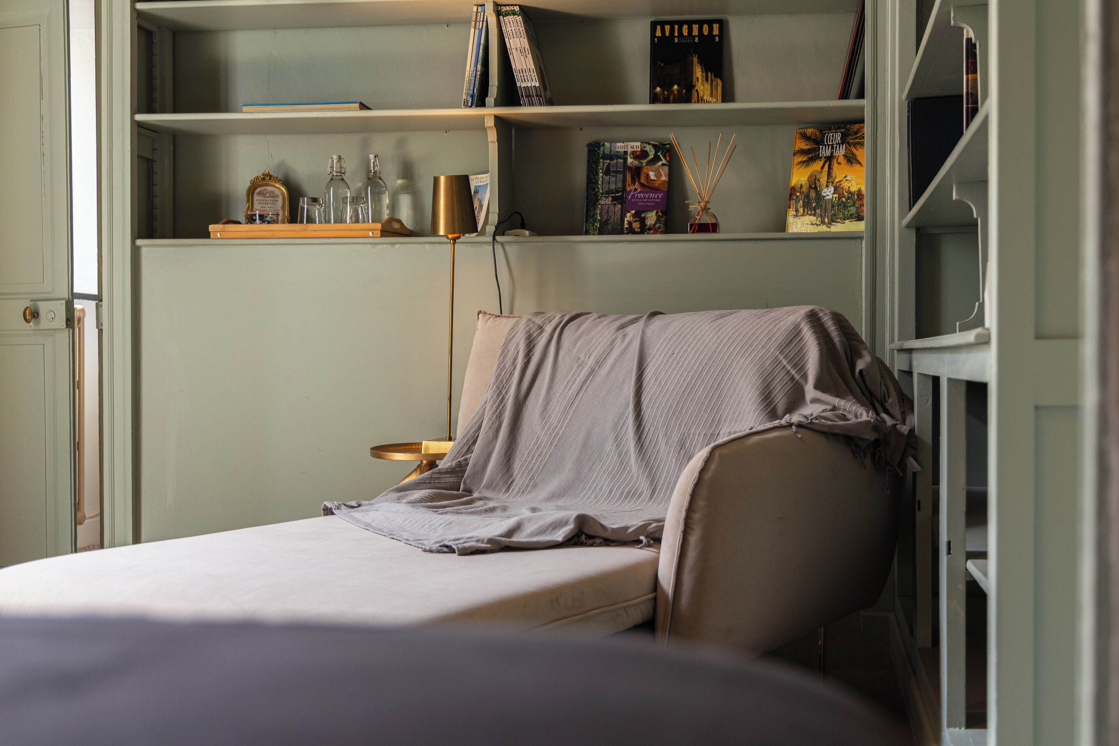 Une chambre à coucher comprenant un lit, une table de chevet, une lampe et des étagères avec des livres et des objets décoratifs.