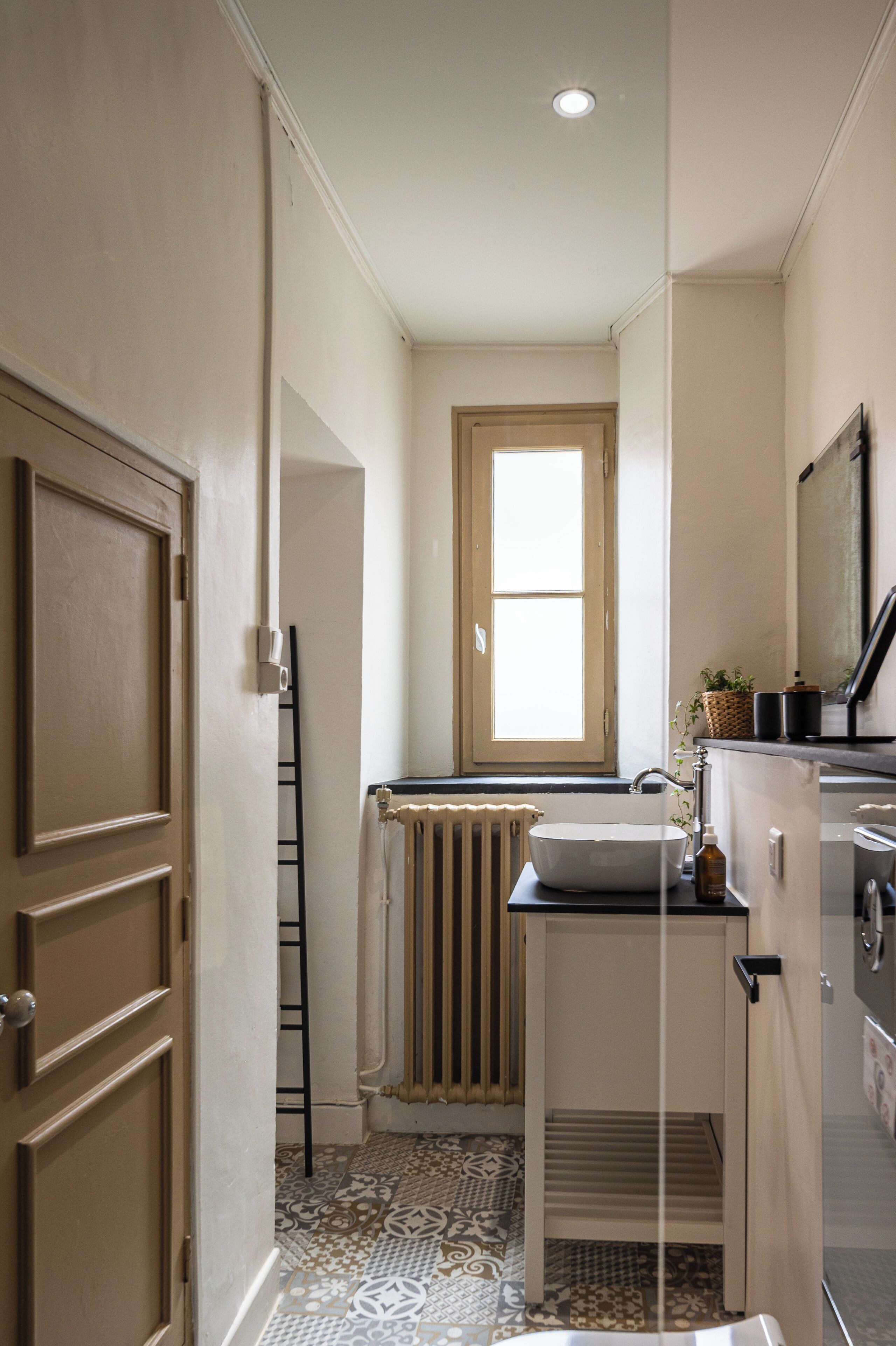 Una cocina estrecha con una ventana, un radiador y un lavamanos.