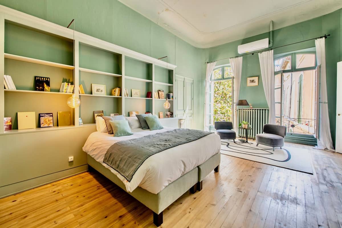 Een slaapkamer met een groot bed, ingebouwde planken, een radiator en uitzicht door een raam met gordijnen.