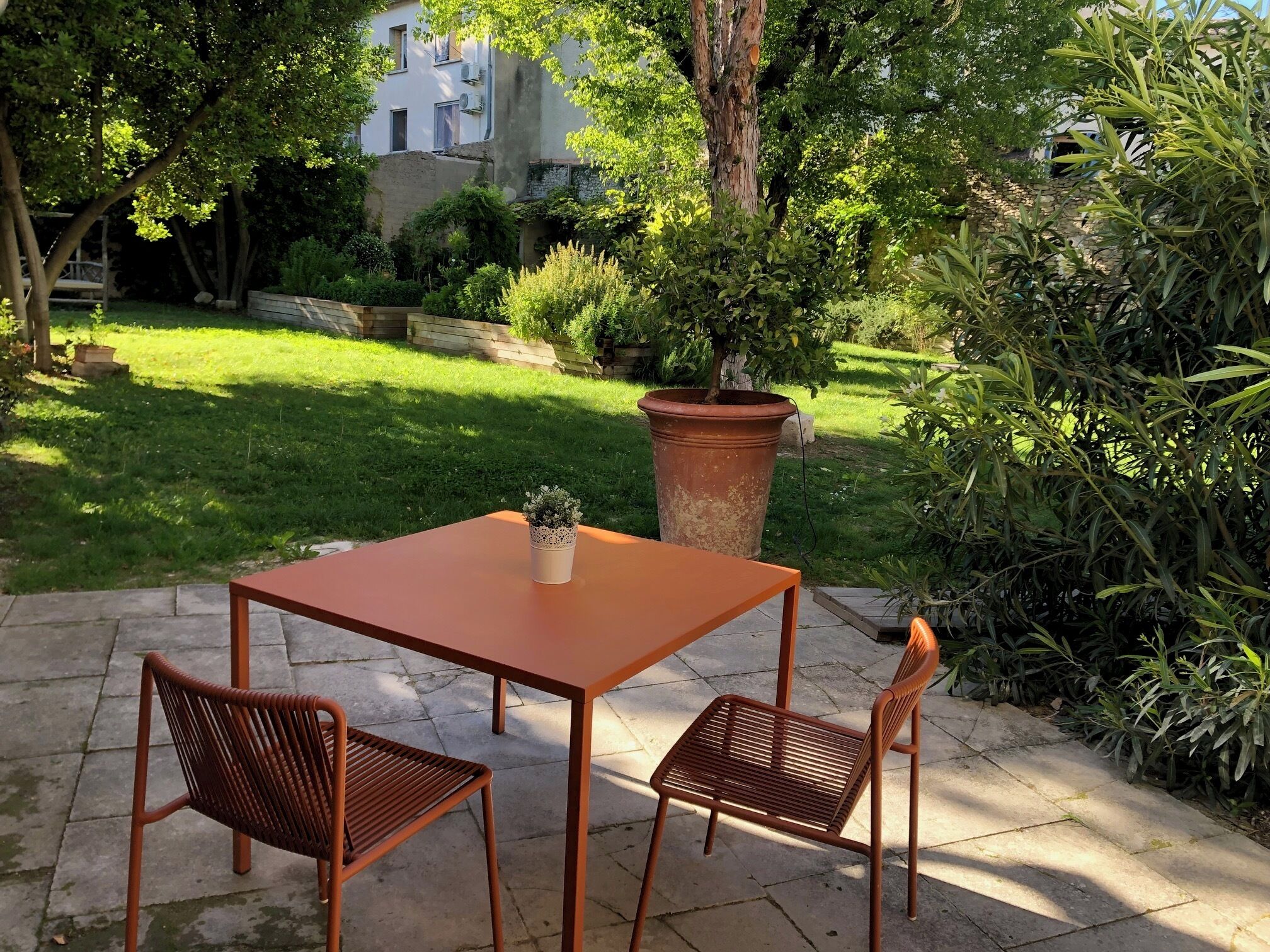 Una terrazza con tavolo e due sedie, circondata da piante e un edificio sullo sfondo.