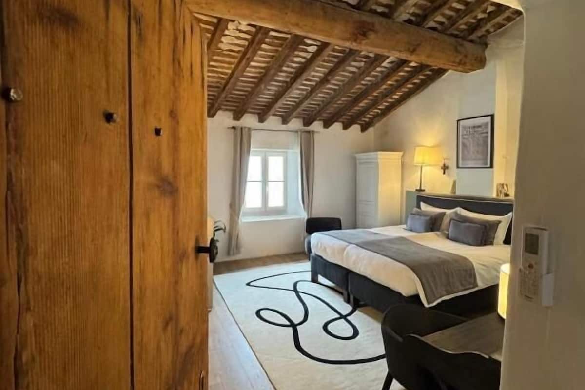 Een slaapkamer met een houten plafond, een bed, een bureau en een stoel.