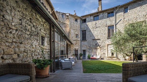 Un patio con edificios de piedra, mobiliario de mimbre y una zona verde.