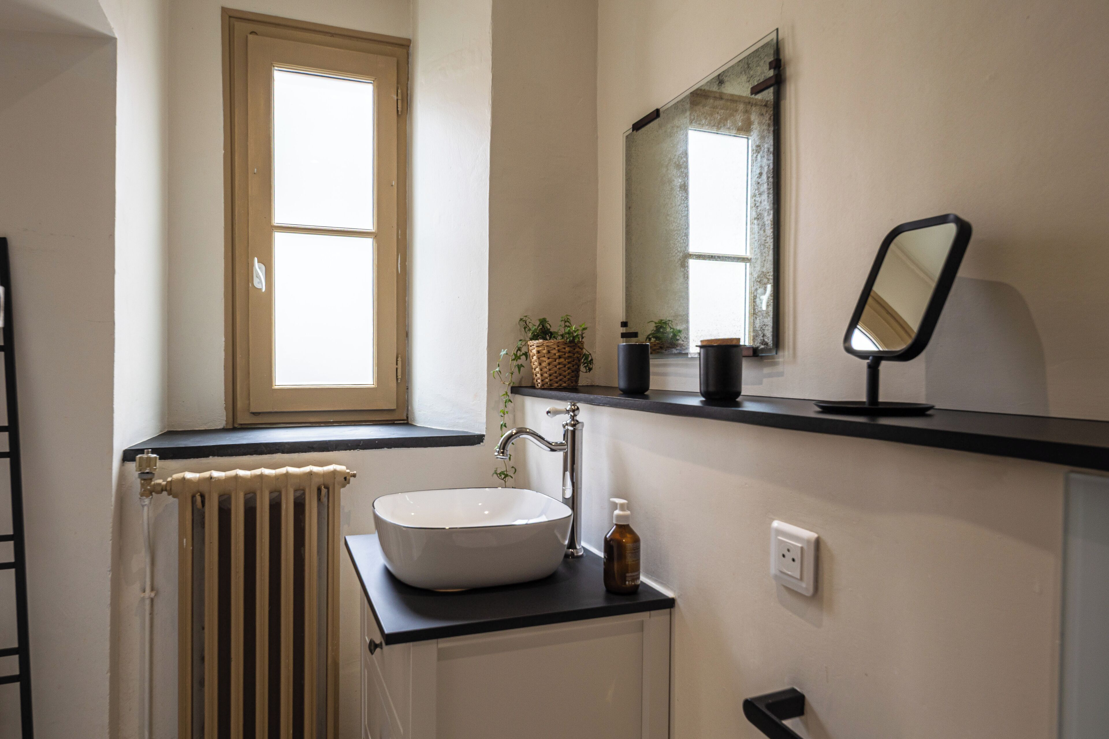 A bathroom with a white sink, a mirror, a window, and a radiator.