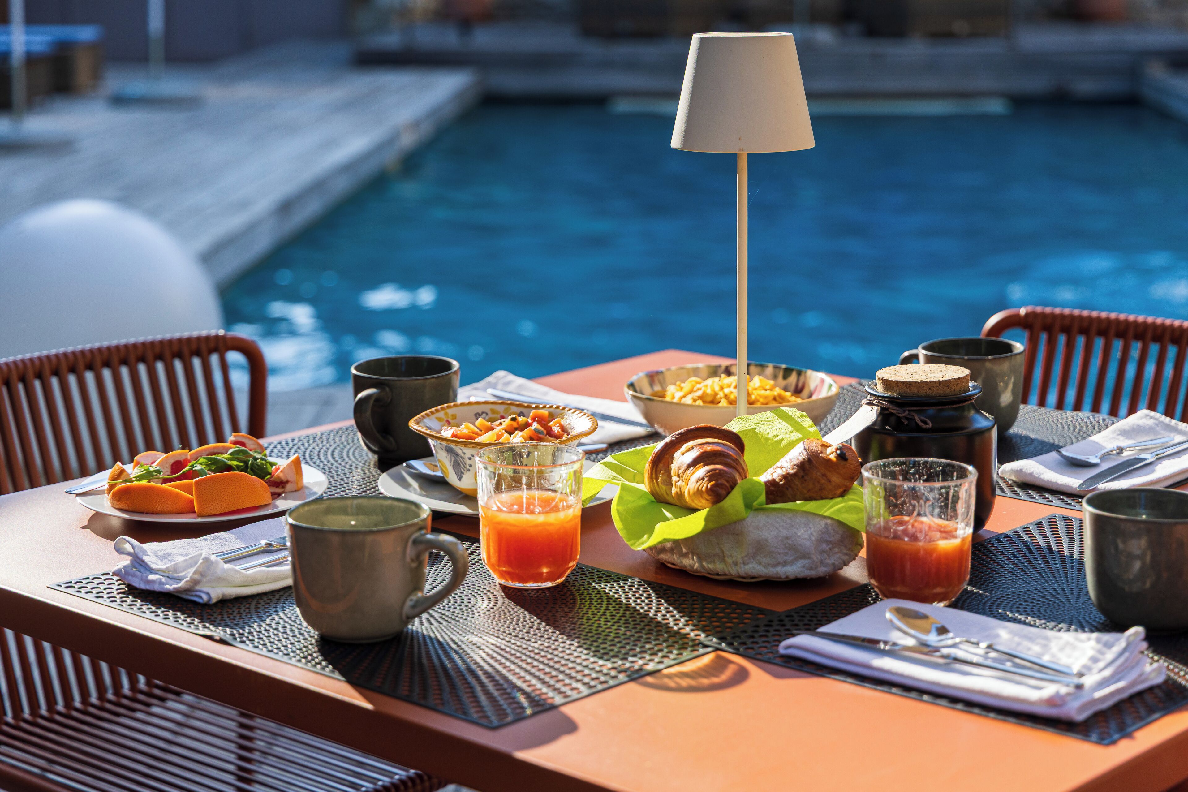 Ein Frühstückstisch mit Croissants, einer Obstschale und einem Glas Orangensaft am Pool.