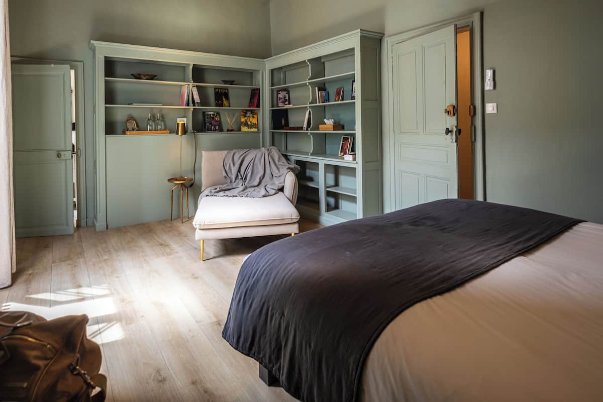 Een slaapkamer met een bed, een stoel, een boekenkast en een kledingkast.
