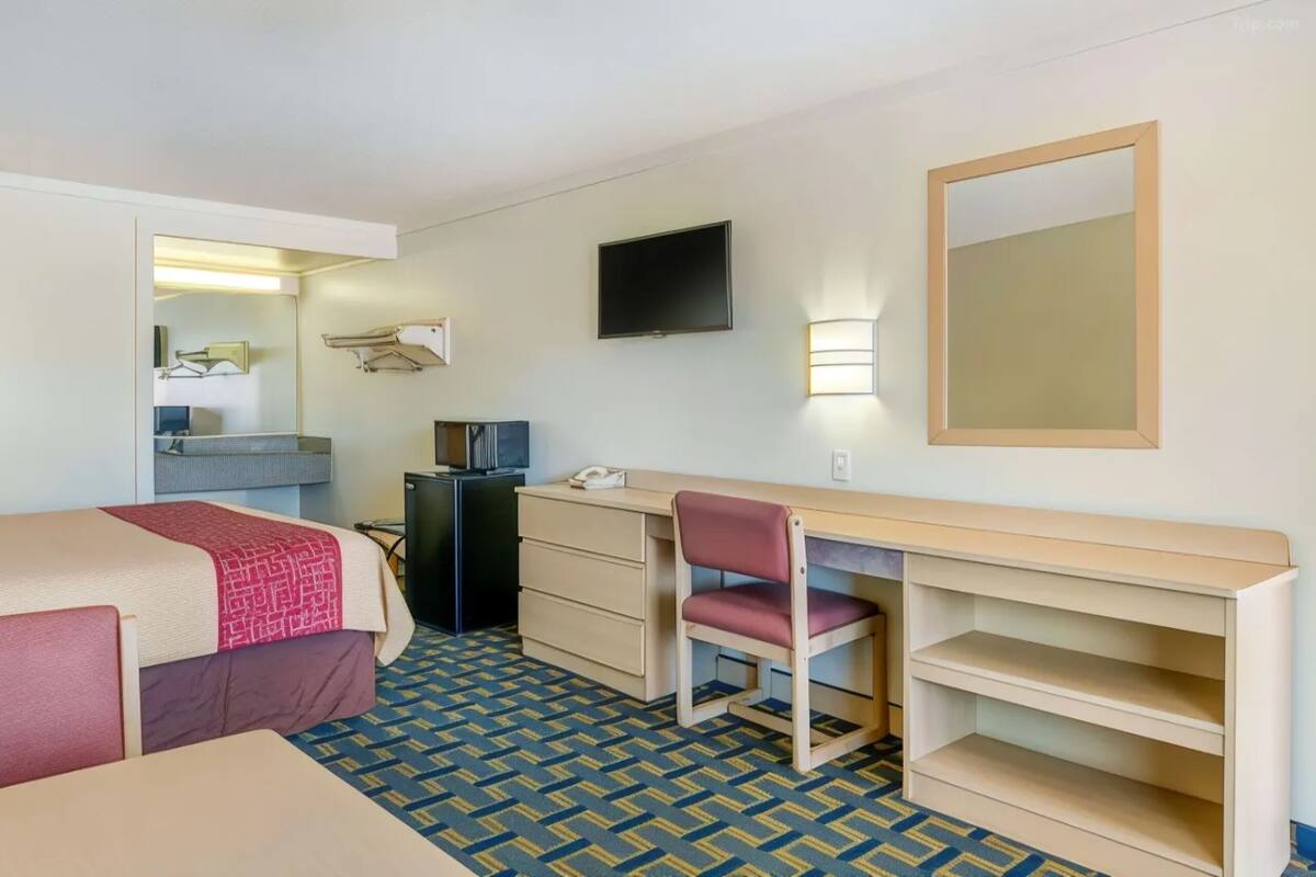 A hotel room with a bed, desk, chair, TV, and a mirror.