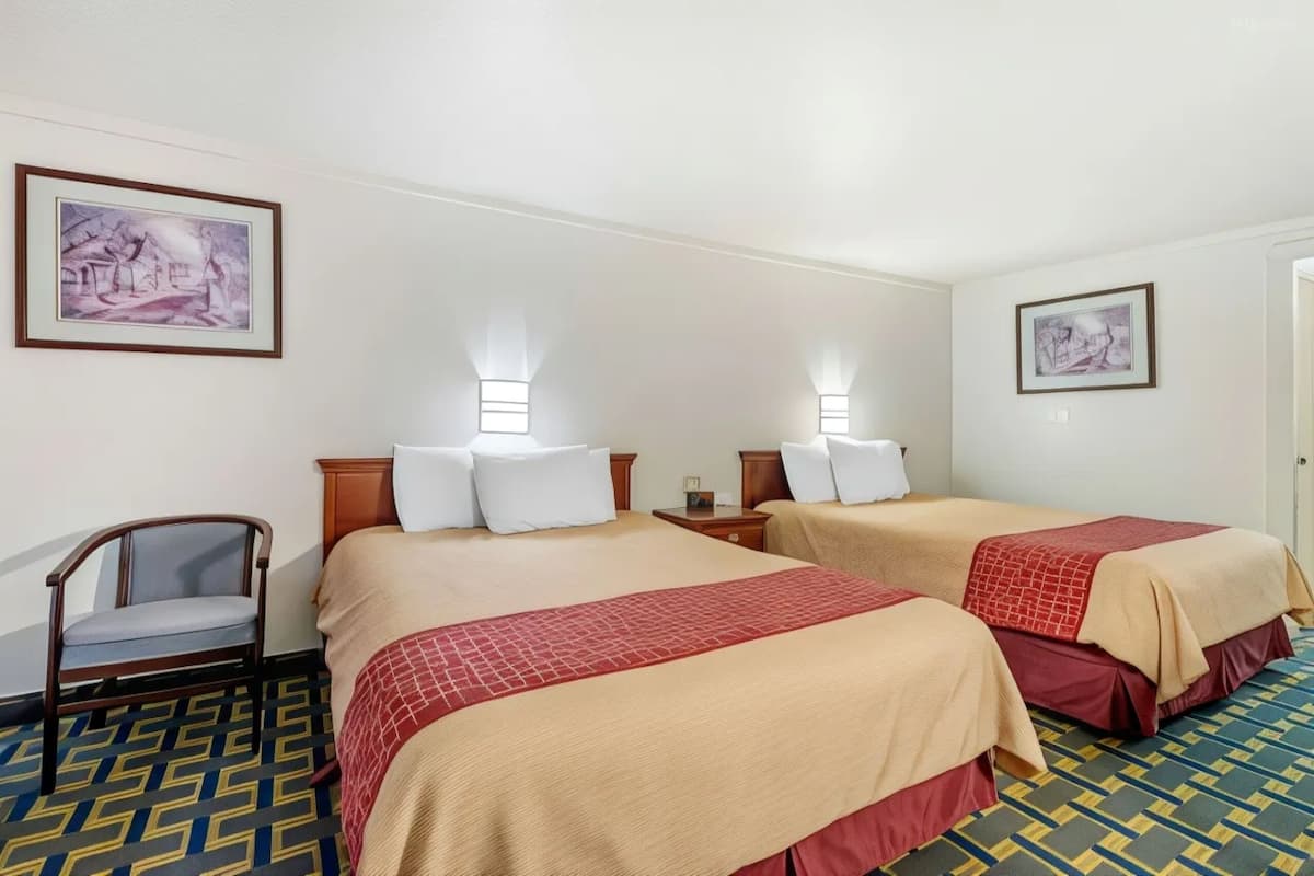 A hotel room with two beds, a chair, and two wall-mounted lamps.