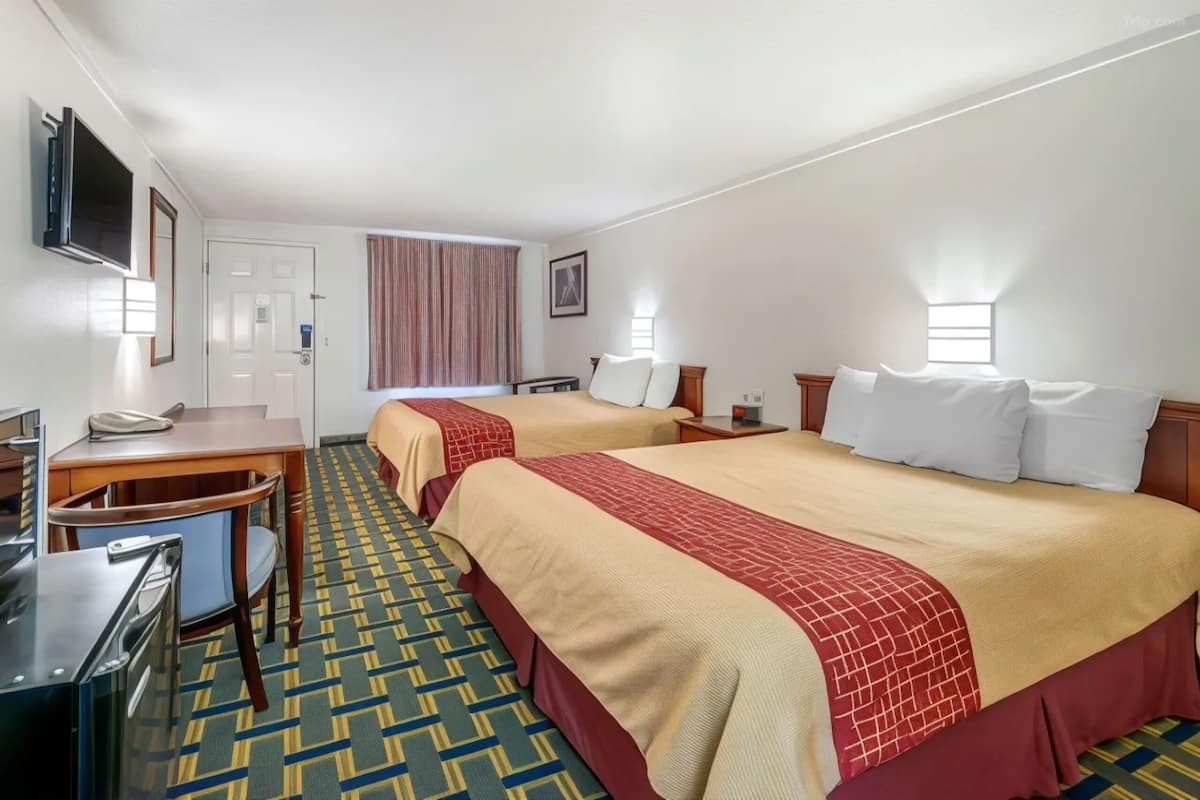 A hotel room with two beds, a desk, a chair, a TV, and a window with curtains.