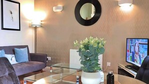 Un salon moderne avec un canapé, une table basse en verre, une plante en pot, un téléviseur à écran plat et un miroir fixé au mur.