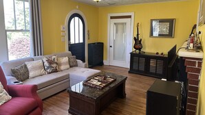A living room with a sofa, a red armchair, a coffee table, a fireplace, a guitar, and a framed picture on the wall. - Newly Renovated 1936 Home Close To Augusta National, Airport & Downtown! (Augusta)