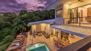 Ein modernes Haus mit Pool, Sitzgelegenheiten im Freien und einem Balkon mit Blick auf eine üppige Landschaft.