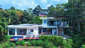 Ein modernes, zweistöckiges Haus mit Pool, umgeben von üppiger Vegetation.