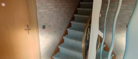A staircase with a wooden door on the left, a framed picture on the wall, and a unique curved wall design on the right.