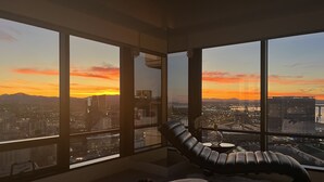 A high-rise room with large windows offering a cityscape view at sunset.