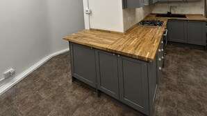 Een moderne keuken met grijze kastjes, een houten aanrechtblad en een inbouwfornuis.