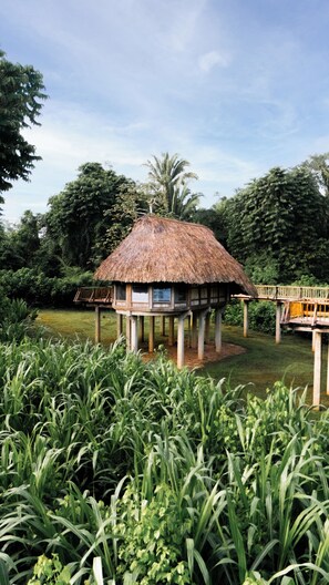 A thatched-roof structure with a wooden deck, surrounded by lush greenery and a clear sky. - Jade Jungle Resort (Teakettle Village)