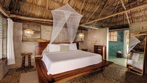 A room with a bed, a wooden headboard, a mosquito net, a small table, and a lamp. - Jade Jungle Resort (Teakettle Village)