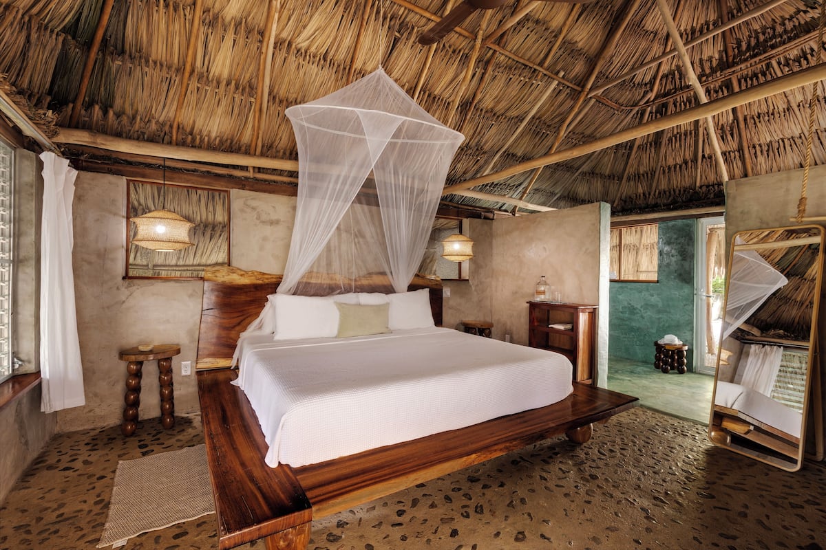 A room with a bed, a wooden headboard, a mosquito net, a small table, and a lamp.