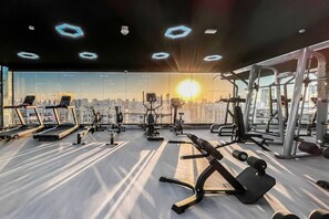 Ein Fitnessstudio mit Trainingsgeräten, großen Fenstern und Blick auf die Stadt.