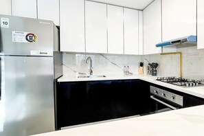 A modern kitchen with a stainless steel refrigerator, a gas stove, and white cabinetry. - Luxe Gardenia 2BR Haven in Dubai (Dubai)